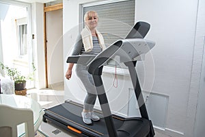 Active senior woman in sportswear using treadmill at home. Coronavirus Covid19 social distance.