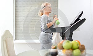 Active senior woman in sportswear walking on treadmill at home