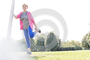 Active senior woman stretching leg in park on sunny day