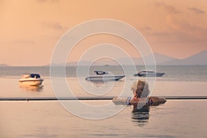 Active senior woman in swimming pool against sea at sunset