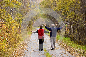 Dos personas de tercera edad (adultos mayores) a pie a través de la caída de las hojas en el país de ruta con los brazos extendidos.