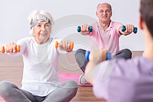 Active seniors during exercises on gym with young instructor