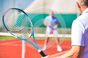 Active seniors playing tennis on sunny day at red court