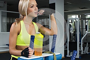 Active sexy blonde woman in sportswear sitting on sport equipment. Gym. Sports nutrition. Amino acids