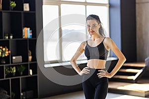 Smiling fitness woman athete in sport bra standing at home window