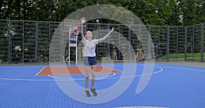 Active smiling teenage girl, fashionable with purple hair, jumping on street basketball court with arms raised