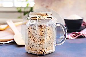 Active sourdough starter in glass jar. Rye leaven for bread and kitchen wooden utensil on rustic background. Close-up. Selective