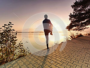 Active sport man runner stretching body on pavement lake side