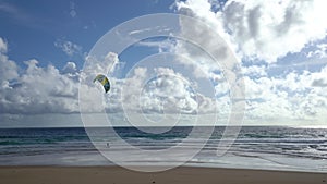 Active sport people practicing kite surfing and windsurfing on deep blue sea water surface with ocean wave crashing on sandy shore