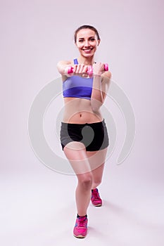 Active sportive athletic woman with dumbbells pumping up muscles biceps