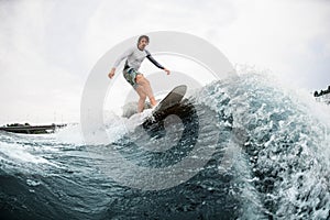 Active sportsman skilfully balancing on wave on wakesurf board.