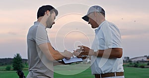 Active sportsmen discuss golf on sunset course. Two golfers talk at country club