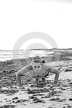 Active sportswoman in sports gear on seashore doing pushups