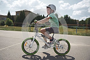Active sporty Caucasian schoolboy, wearing sports helmet cycling on a bicycle on the asphalt road in urban environment