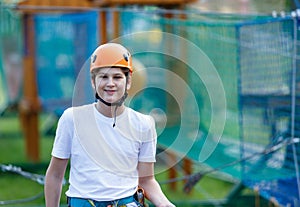 Active sporty kid in helmet doing activity in adventure park with all climbing equipment. Active children climb on the trees