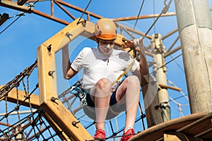 Active sporty kid in helmet doing activity in adventure park with all climbing equipment. Active children climb on the trees