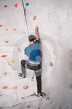 Active sporty man practicing rock climbing on artificial rock in a climbing wall