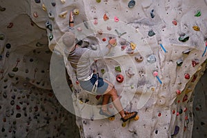 Active sporty man wearing protective face mask and a hat practicing rock climbing on artificial rock in a climbing wall
