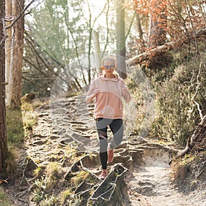 Active sporty woman listening to the music while running in autumn fall forest. Female runner training outdoor. Healthy