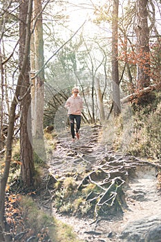 Active sporty woman listening to the music while running in autumn fall forest. Female runner training outdoor. Healthy