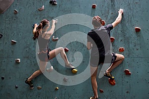 Active sporty woman and man practicing rock climbing on artificial rock