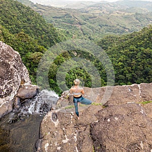 Active sporty woman relaxing in nature, practicing yoga on high clif by 500 feet waterfall at Black river gorges