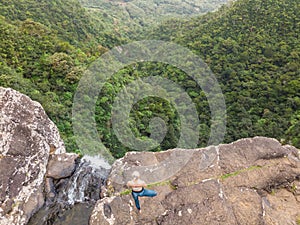 Active sporty woman relaxing in nature, practicing yoga on high clif by 500 feet waterfall at Black river gorges