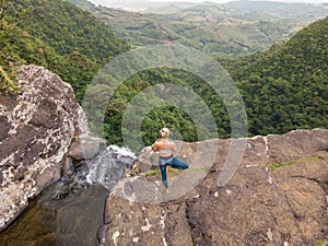 Active sporty woman relaxing in nature, practicing yoga on high clif by 500 feet waterfall at Black river gorges