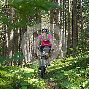 Active sporty woman riding mountain bike on forest trail .