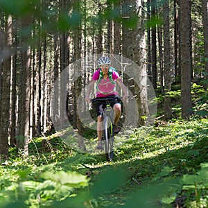 Active sporty woman riding mountain bike on forest trail .