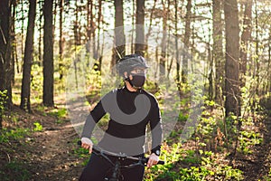 Active sporty woman riding mountain bike on forest trail, wearing a face mask against air pollution and coronavirus.