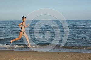 Active sporty woman run along ocean surf by water pool to keep fit and health. Sunset black sand beach background with