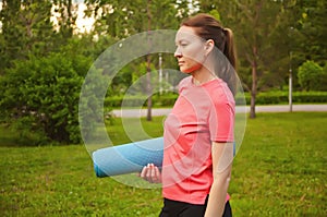 Active sporty woman training outdoors. Female stanging in a park and holding sport mat photo