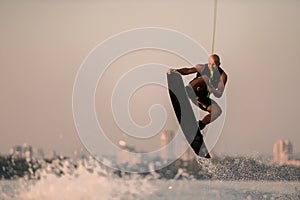 active strong man holds cable and skilfully making jump showing trick on wakeboard on sky background.