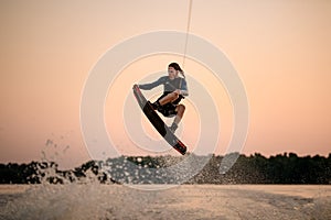 active strong man making trick in jump time with wakeboard on sky background.