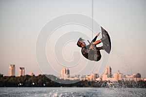 active strong man rider holds rope and skilfully making extreme jump showing trick on wakeboard.