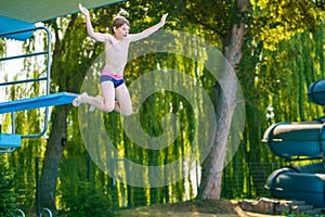 Active teenager boy jumping into an outdoor pool from spring board or 5 meters diving tower learning to dive during