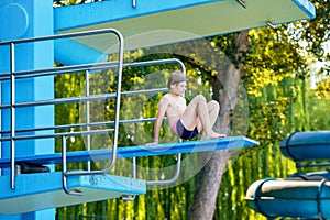 Active teenager boy jumping into an outdoor pool from spring board or 5 meters diving tower learning to dive during