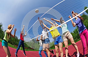 Active teenagers playing volleyball on game court