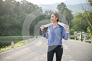 Active and tired Asian woman in sportswear stands on the street, holding a towel