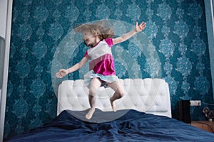 Active toddler girl dancing in bed baby jumping on white and blue bed blur background. what to do in quarantine