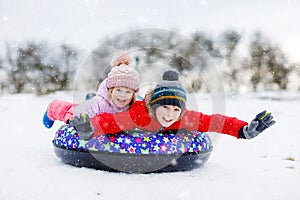 Active toddler girl and school boy sliding together down the hill on snow tube. Happy children, siblings having fun