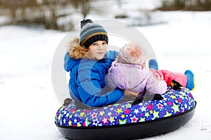 Active toddler girl and school boy sliding together down the hill on snow tube. Happy children, siblings having fun