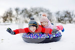 Active toddler girl and school boy sliding together down the hill on snow tube. Happy children, siblings having fun