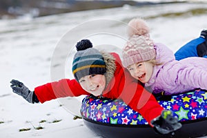 Active toddler girl and school boy sliding together down the hill on snow tube. Happy children, siblings having fun