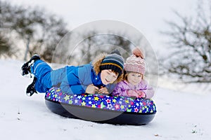 Active toddler girl and school boy sliding together down the hill on snow tube. Happy children, siblings having fun