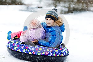 Active toddler girl and school boy sliding together down the hill on snow tube. Happy children, siblings having fun