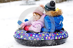 Active toddler girl and school boy sliding together down the hill on snow tube. Happy children, siblings having fun