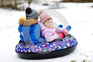 Active toddler girl and school boy sliding together down the hill on snow tube. Happy children, siblings having fun