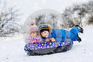 Active toddler girl and school boy sliding together down the hill on snow tube. Happy children, siblings having fun